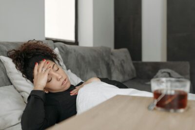 Woman lying on a couch appearing unwell, possibly experiencing a headache or illness.