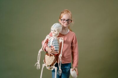 A smiling young girl with glasses holding an anatomical skeleton model for educational purposes.