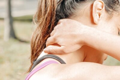 A woman massages her neck outdoors, relieving discomfort and tension.