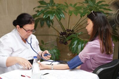 A healthcare worker measures a woman's blood pressure in an outdoor setting, emphasizing wellness and care.